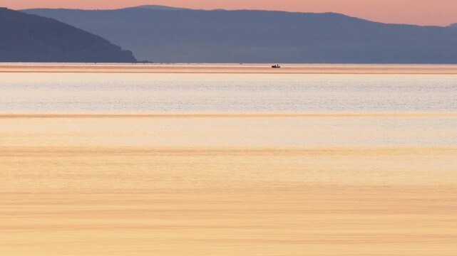 Sunset on Lake Baikal in Russian Siberia on a chilly autumn evening. The orange sky is reflected in the calm surface of the lake.