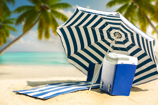 Beach umbrella and portable cooler placed on hot sandy beach under bright sunlight. The scene captures relaxed summer atmosphere with clear blue sky and seaside vibes. Summer and vacation concept.