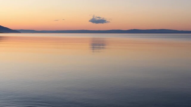 Sunset on Lake Baikal in Russian Siberia on a chilly autumn evening. The orange sky is reflected in the calm surface of the lake.