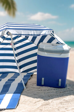 Beach umbrella and portable cooler placed on hot sandy beach under bright sunlight. The scene captures relaxed summer atmosphere with clear blue sky and seaside vibes. Summer and vacation concept.