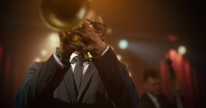 Black Male Trumpeter in Glasses Performs a Soulful Jazz Song Live With His Band on a Bar Stage, Playing an Energetic Concert Set as the Audience Enjoys the Intimate Music Event.