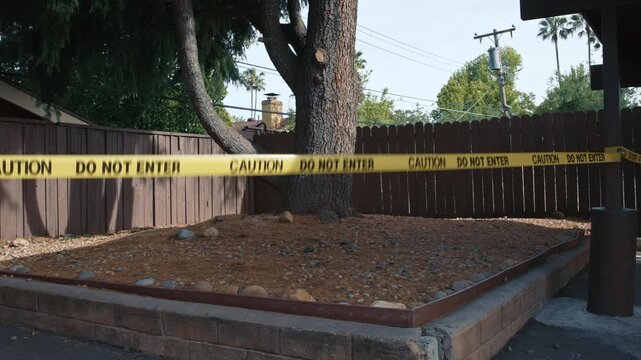 Yellow caution tape do not enter enclosing unsafe fenced area with tree daytime showing restricted access zone safety and perimeter control in outdoor environment
