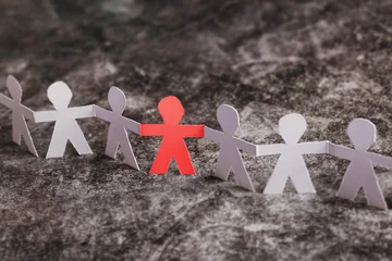 Inclusivity concept, outcast in group of people, paper humans holding hands together, one red © Song_about_summer