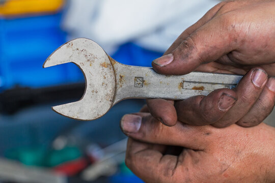 Worker holds a rusty wrench in a repair shop while tools are visible in the background during the day