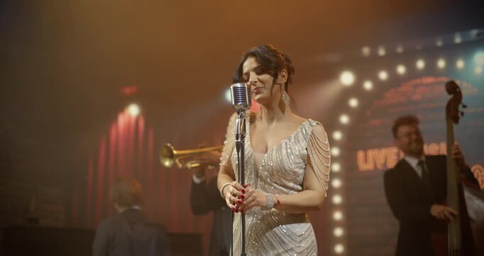 Portrait of a Female Singer Performing Live Jazz Song With Band on Stage at a Bar Concert Event, Singing to the Audience as Musicians Play Piano, Trumpet, Bass and Sax Music All Night.