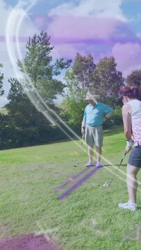 Vertical video: Woman lining up and taking golf shot while partner watching, streaks crossing club
