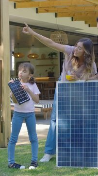 Vertical video: Reaching for mini panel, mom showing kid pointing up to sun at patio by big panel