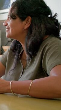 Vertical video: After hearing offframe voice, woman in olive shirt sipping mug at kitchen table