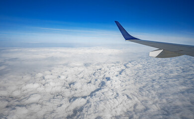 Obraz premium An aerial view from an airplane window shows a silver wing soaring above a thick blanket of white clouds under a clear blue sky.