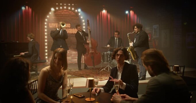 Four Young Adult Friends Relax at a Small Table in a Live Jazz Bar, Chatting, Smiling and Raising Drinks While the Band Plays Nearby, Fun Night of Music, Friendship and Connection.