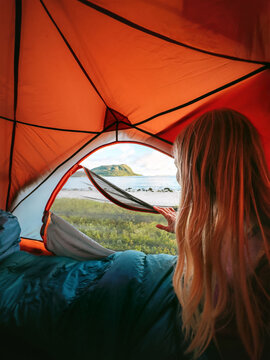 Woman inside tent looking at the view from the entrance - travel lifestyle summer camping vacations outdoor, tourist girl solo on adventure trip weekend getaway in the wild