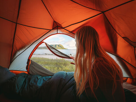 Woman wakes up inside a tent and looks at the sea through the entrance on solo camping trip, travel lifestyle summer vacations outdoor girl traveler enjoying perfect morning adventure tourism freedom