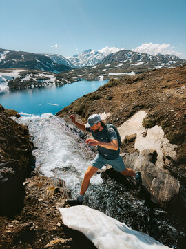 Man hiking solo in Norway travel trail running adventure in the great outdoors - active hiker traveler crossing river in Lahko park, healthy lifestyle summer vacations endurance energy freedom concept