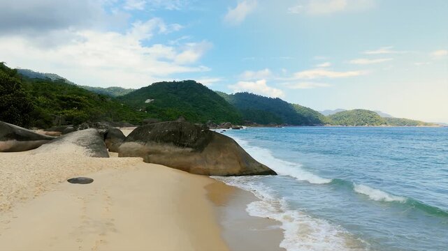 Cepilho Beach with white sand, rocks, boulders and turquoise ocean waves with people walking in Trindade, Paraty, Brazil. Push in and crane up camera movement