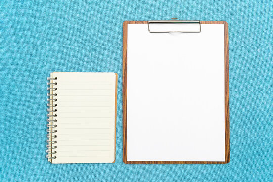 Notebook and white report papaer on wooden clipboard on blue fabric background, education and business object