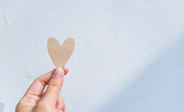 Wooden heart in girl hand with space on white cement wall background, love and romance symbol, valentine background idea