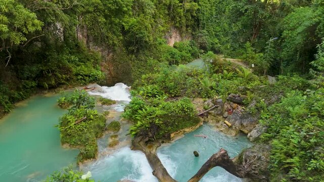 Aerial reveal shot over wild upper tier pools of Kawasan Falls Cebu Philippines showing multiple turquoise pools connected by white cascading water over limestone terraces dense jungle ferns and canyo
