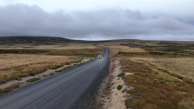 Cinematic aerial view of a car driving through remote coastal landscape in the Falkland Islands, tracking drone footage.
