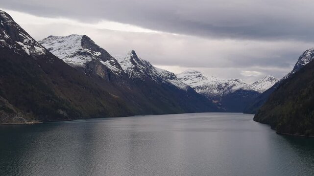 Snow-dusted peaks frame a tranquil Norwegian fjord under overcast skies. Ideal for travel and nature content.