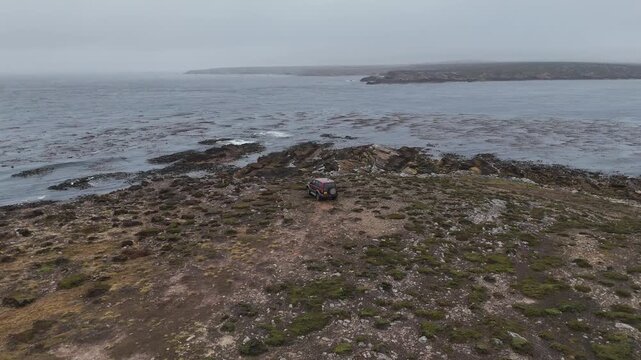 Drone shot of a vehicle along rocky coastal terrain with ocean backdrop in the Falkland Islands. Descending aerial footage.
