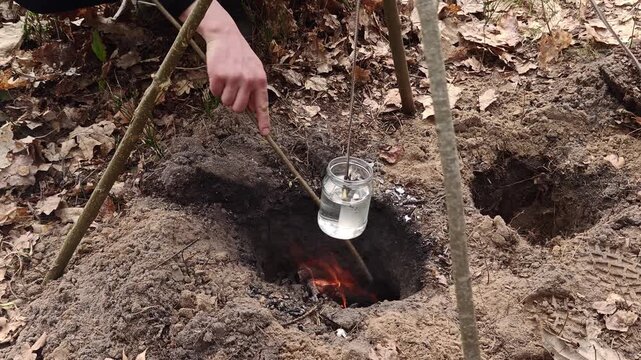 Placing a glass jar with water into a dakota fire hole for primitive cooking