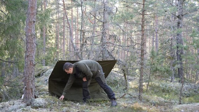 Man setting up tarp shelter in a pine forest wilderness campsite
