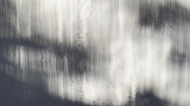 abstract monochrome light reflection shimmers along textured gray concrete wall casting ethereal dark shadow