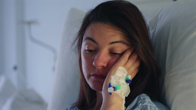 Close up of female patient face resting on hand with intravenous catheter, eyes heavy and expression subdued, conveying emotional fatigue, recovery and vulnerability