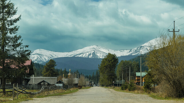 Remote mountain village with snow-capped peaks under a dramatic cloudy sky