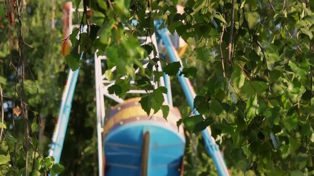 Large boat swing in an amusement park emerges from the lush greenery,