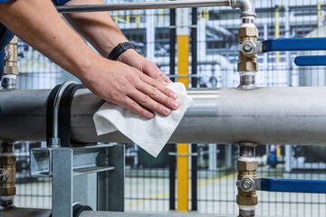 Worker meticulously cleans a stainless steel pipe with a white cloth in an industrial facility