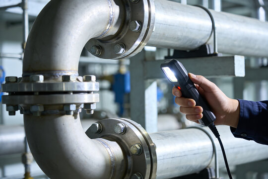 Industrial pipe inspection with a flashlight, checking for leaks and damage in a factory setting