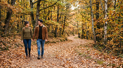 Obraz premium Happy Couple Hold Hands on an Autumn Day Walk Through a Romantic Forest Path Covered with Fallen Leaves. Autumn concept
