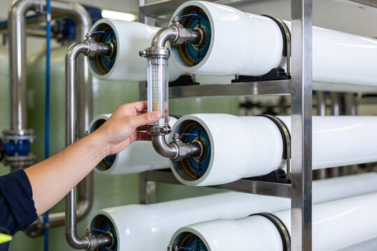 Technician inspecting industrial water filtration system with flow meter and membrane housings