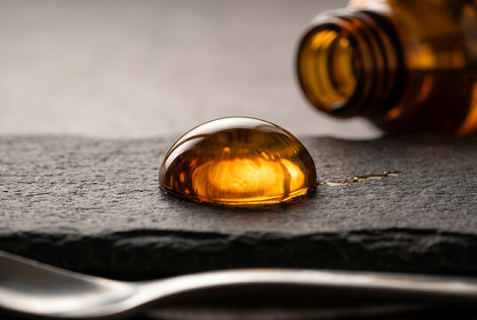 A single golden oil droplet with perfect surface tension on a dark slate edge. A minimalist metaphor for precision, purity, and concentrated luxury for elite branding.