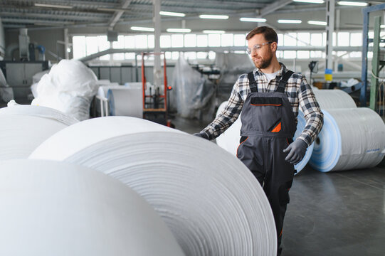 Worker moving polypropylene fabric rolls in factory