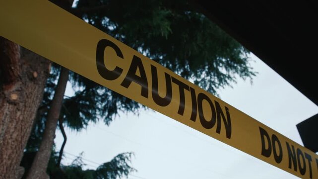 Yellow caution tape do not enter against sky and trees daytime shows restricted access area safety and perimeter control in outdoor environment
