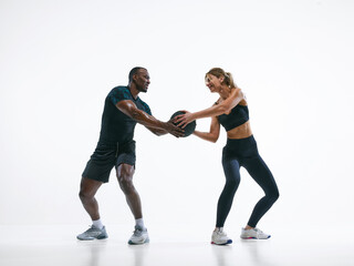 Fototapeta premium Fitness couple passing medicine ball in functional training workout on white background. Concept of workout routine, team fitness training, motivation support, coordinated movement, healthy lifestyle