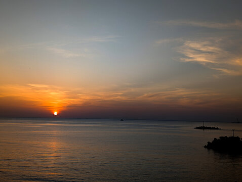 Golden hour sunset over calm ocean waters with sun reflecting on the surface.