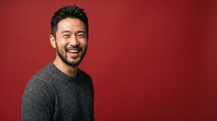 Obraz premium A portrait of a cheerful East Asian man with a beard, laughing joyfully against a solid vibrant red background