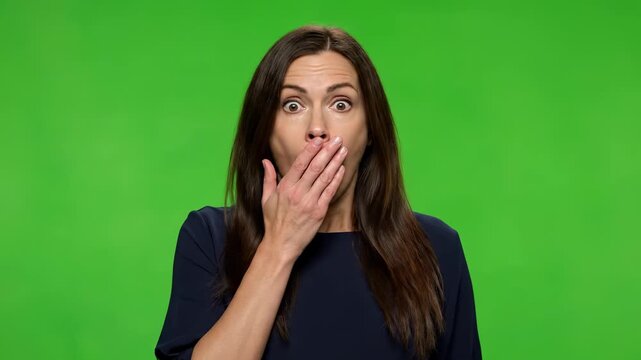 Astonishment Unveiled: A woman with wide eyes and a hand covering her mouth expresses shock and amazement against a vibrant green backdrop, capturing a moment of surprise.