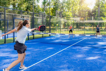 Obraz premium Padel player hitting forehand during outdoor doubles game, dynamic action with visible opponents and court environment.