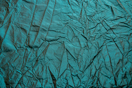 Wrinkled turquoise silk taffeta fabric background with folds and crisp woven sheen.