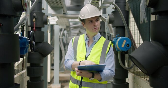 A male engineer conducts a routine inspection of an industrial HVAC system in a plant room, checking machinery for performance and safety compliance.