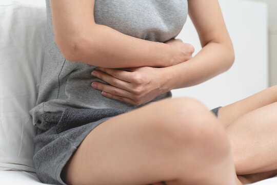 Menstruation symptom concept, Close-up woman touching her belly and feeling stomach pain from cycle period on the bed at home.