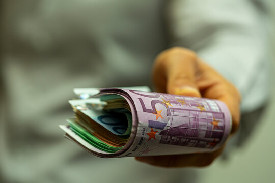 Close up of a hand holding a bundle of rolled euro banknotes and cash money