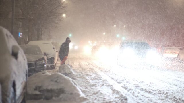 Person shoveling snow on a busy street during blizzard
