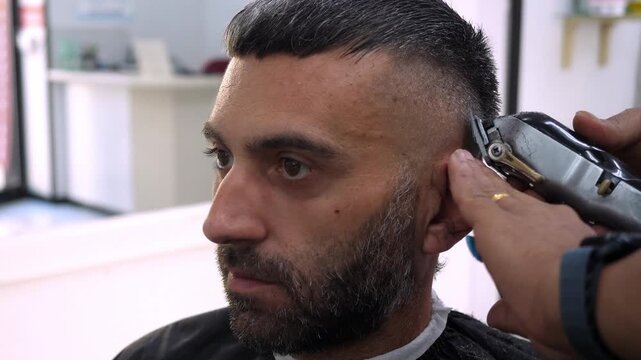 Professional barber uses clipper on a young mans hair. The action highlights efficiency, precision, and attention to detail in modern grooming.