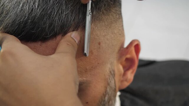 Barber refines beard edges with a razor on a young man. The scene emphasizes finishing touches, precision, and attention to detail in professional grooming