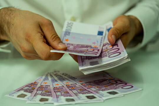 Close up of a man's hands counting a large wad of five hundred euro bills.